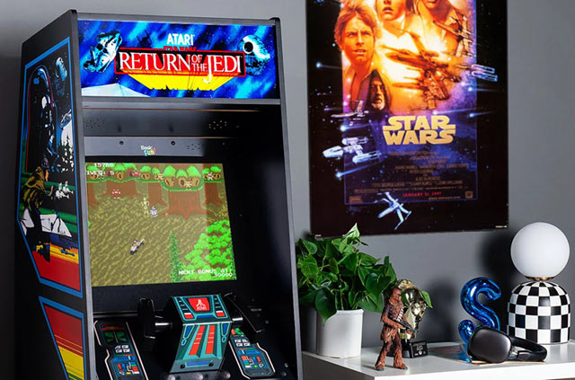 Le haut de la borne d'arcade Star Wars avec son marquee "Return of the Jedi" à côté d'un poster du film original et de divers objets dont une figurine de Chewbacca