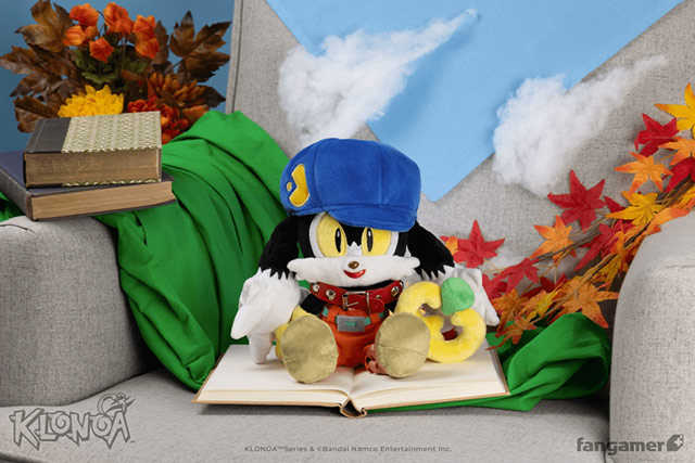 Une peluche Klonoa assise sur un canapé devant un décor de nuages en coton et de feuilles d'automne