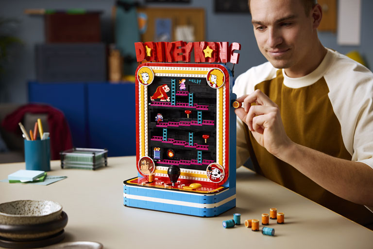 Une mini borne tabletop Donkey Kong en LEGO, avec un utilisateur insérant un tonneau sur le côté