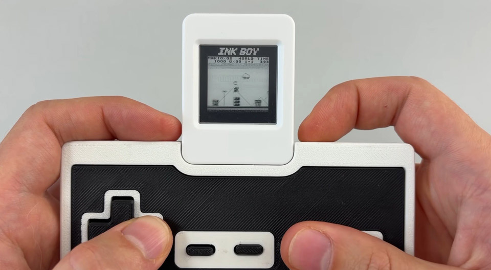 Les mains d'un joueur reposant sur une manette type NES surmontée d'un tout petit écran monochrome mais très fin